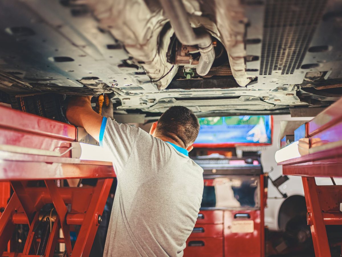 Mechaniker arbeitet unter einem angehobenen Fahrzeug an der Karosserie